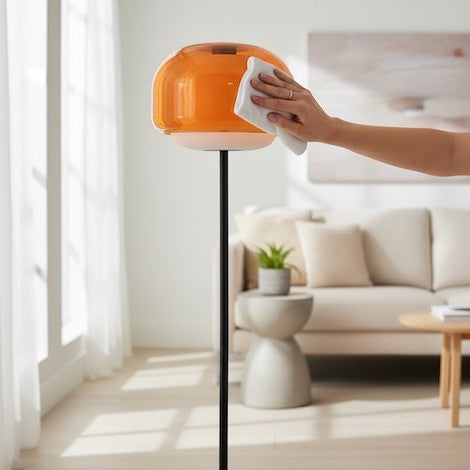 A person gently cleaning a glass floor lamp shade with a microfiber cloth.