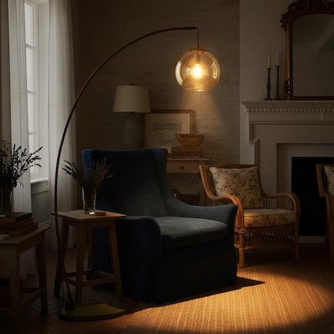 An arched floor lamp with an amber glass shade showing 360-degree light distribution in a dark room.