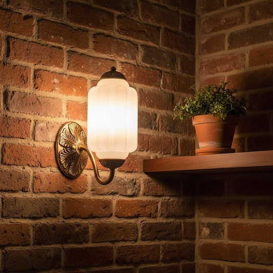 A vintage milk glass and oiled brass wall sconce mounted on a rustic exposed brick wall, illustrating the mix of textures.