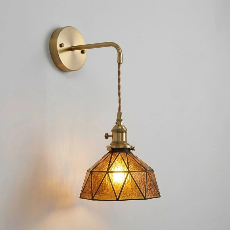 Wall-mounted brass light fixture with geometric glass shade on a plain background