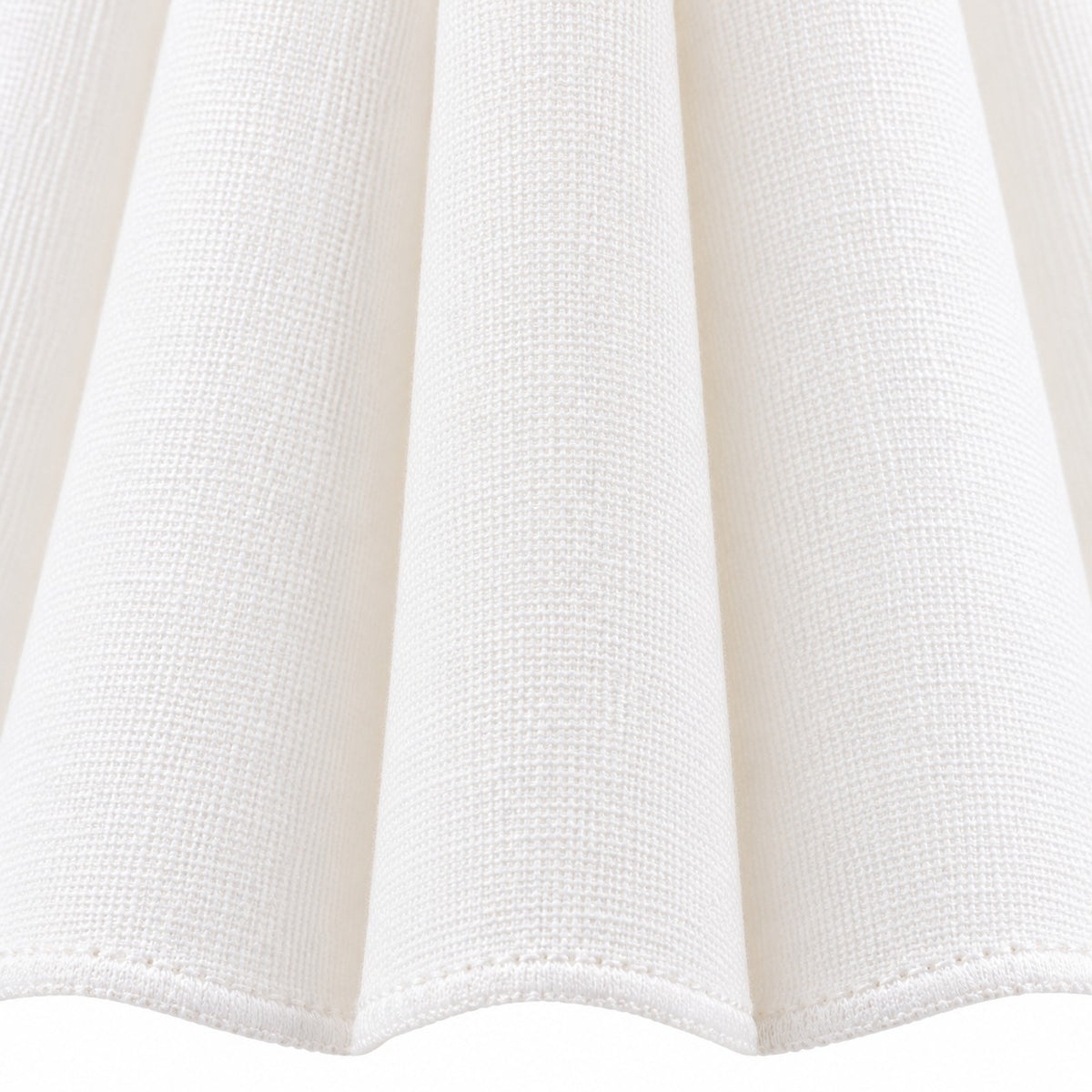 Close view of the white cotton shade fabric, vertical pleats, and stitched scalloped hem