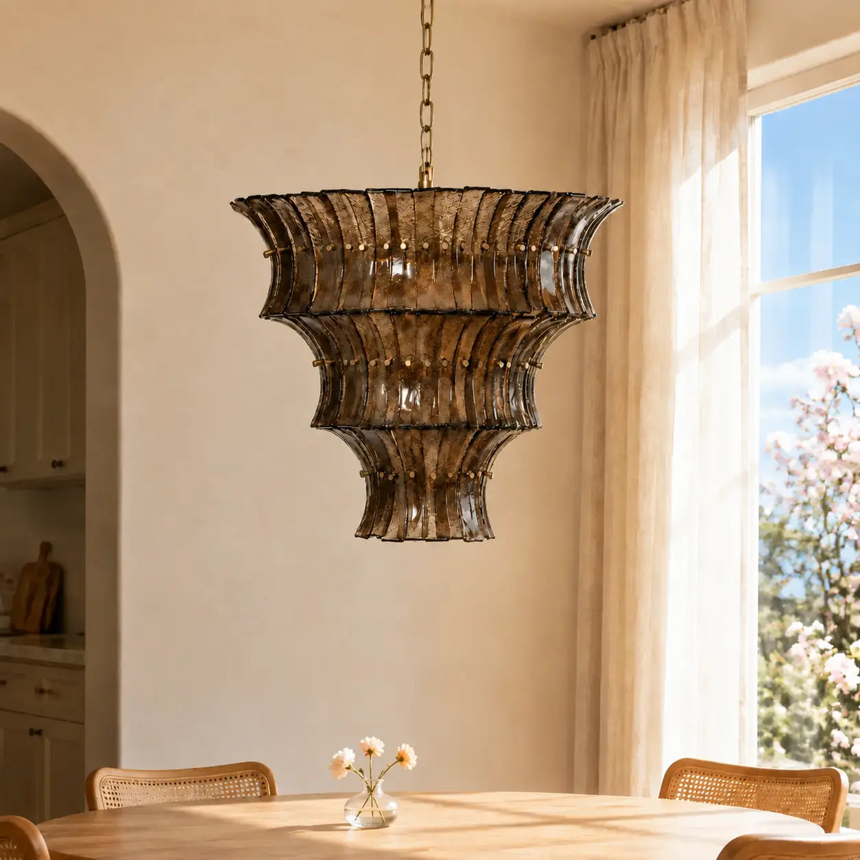 Smoked amber textured glass tiered chandelier above a round dining table with a petite floral accent