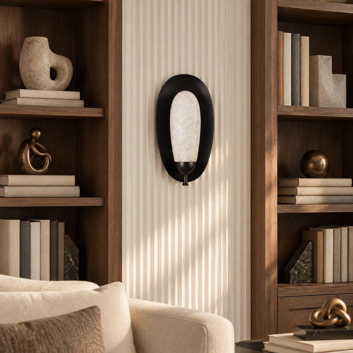 Black alabaster Maelle wall sconce between art-filled bookshelves